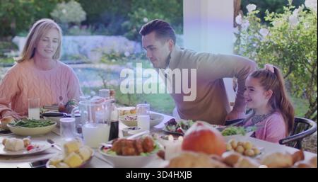 Gathering family sitting at table on porch, pink-sweater woman, man leaning, roast-chicken Stock Photo