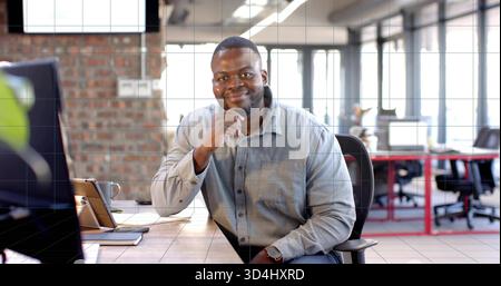 Leaning man wearing grey shirt and watch, smiling at camera at open-plan office desk with monitor Stock Photo