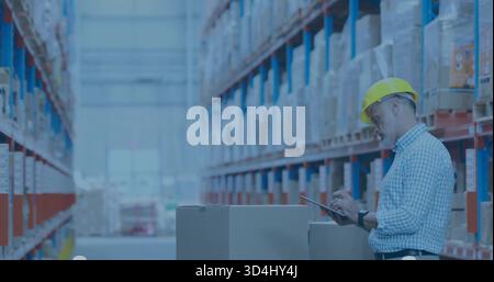 Inspecting warehouse manager wearing yellow hard hat, shirt, using tablet by boxes, copy space Stock Photo