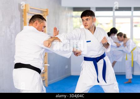 Young male attendee of karate classes fighting with middle-aged man in sports hall Stock Photo