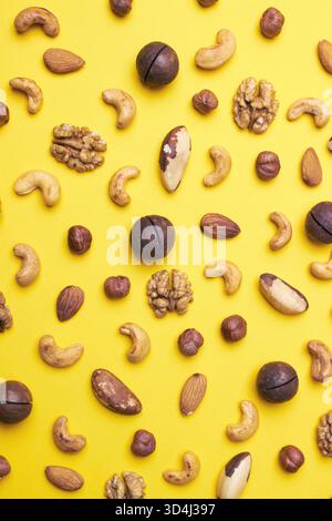 Pattern of nuts mix. Hazelnut, macadamia, almonds, walnut, cashew, brazil nut, on yellow background. Top view. Stock Photo