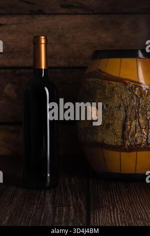A striking black wine bottle stands next to a charming barrel decorated with natural wood details, all set against a backdrop of warm wooden tones Stock Photo