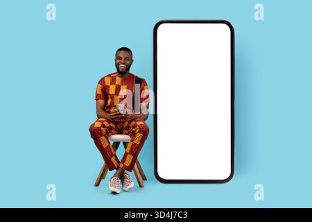 Black Man With Smartphone Sitting On Chair Near Big Blank Phone Stock Photo