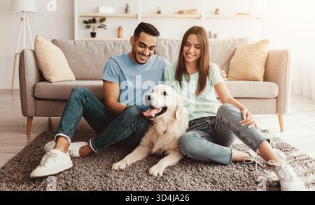 Happy Couple Relaxing With Their Golden Retriever in Cozy Living Room Stock Photo