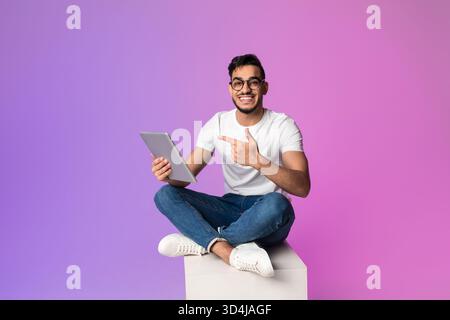 Handsome Millennial Arab Man Engages With Digital Tablet in Neon Light Setting While Sitting Stock Photo