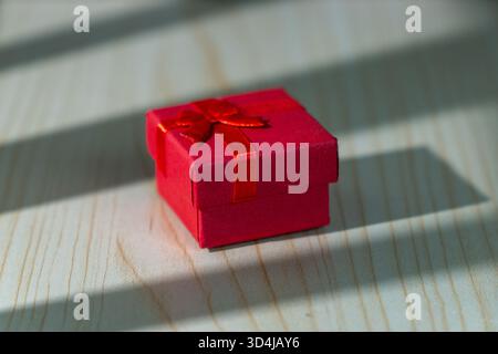 Small red gift box with ribbon placed on a wooden table. Concept of surprise, celebration, and minimalism. Stock Photo