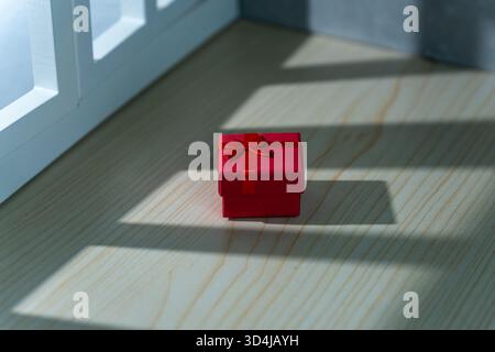 Small red gift box with ribbon placed on a wooden table. Concept of surprise, celebration, and minimalism. Stock Photo