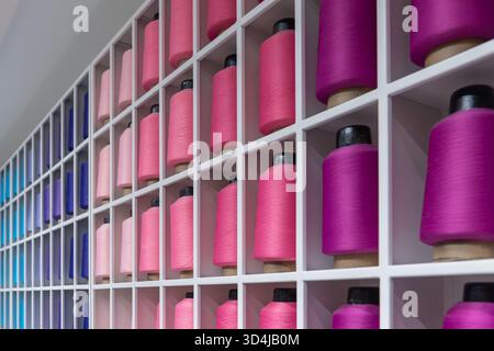 Colorful spools of thread arranged neatly on a shelf. Concept of textile manufacturing, fashion, and raw materials. Stock Photo