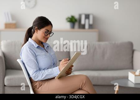 Professional Psychologist Conducts Counseling Session While Taking Notes in Modern Office Setting Stock Photo