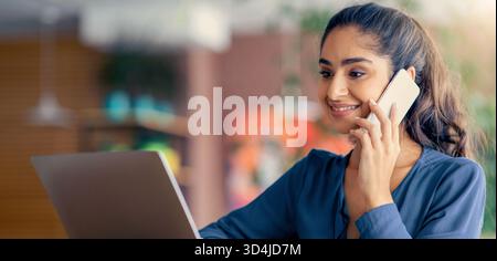 Young Professional Engaged in a Phone Call While Working on a Laptop in an Office Setting Stock Photo
