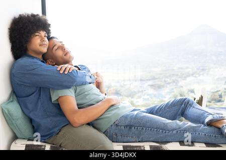 Relaxing Diverse male partners leaning on bench by large window with teal pillow, copy space Stock Photo
