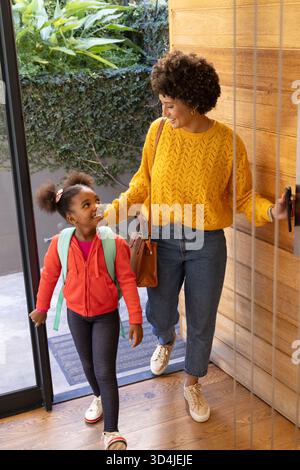 Holding glass-and-metal door open Diverse mother and daughter standing in entryway, with doormat Stock Photo