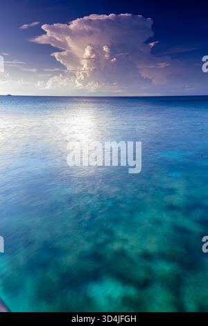 A vertical, long-exposure photograph of the ocean, showing smooth, clear turquoise water, with a large, dramatic cloud in the sky at twilight. Stock Photo