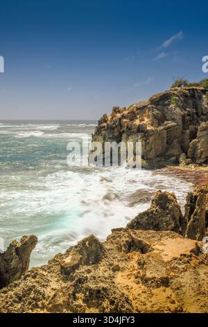 A long exposure captures the motion of white waves crashing against rugged, golden-brown volcanic rock cliffs on the coast of Kauai, Hawaii, under a c Stock Photo