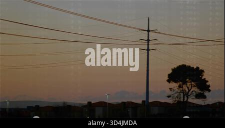 Framing utility pole with crossarms and power lines against suburban dusk sky, lit streetlights Stock Photo