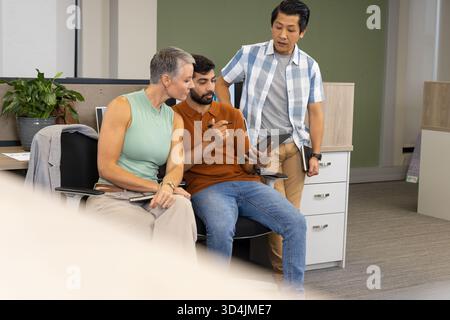 Collaborating diverse coworkers analyzing data on tablet in modern open-plan office, with stylus Stock Photo