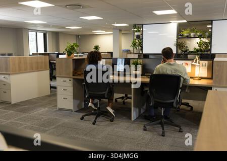 Collaborating Diverse coworkers typing and calling at open-plan office desks, with dual monitors Stock Photo