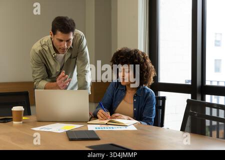 Analyzing diverse coworkers reviewing bar and pie charts in meeting room, with open silver laptop Stock Photo