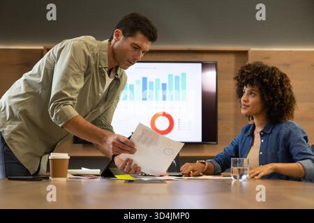 Diverse coworkers presenting charts, reviewing data on screen in meeting room, with coffee cup Stock Photo