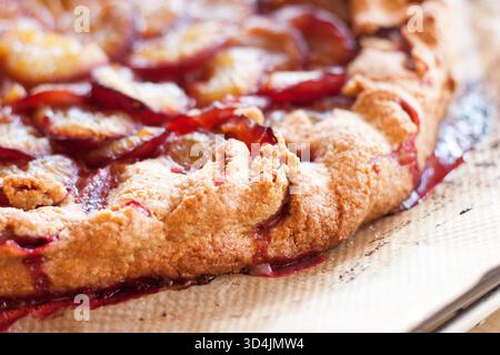 Close-up of a rustic, homemade plum (Zwetschgen) galette or open-faced tart, freshly baked on parchment paper on a baking tray. Stock Photo