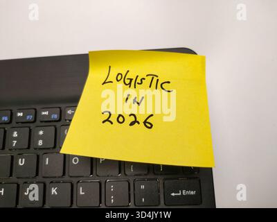The image shows a yellow sticky note on a black computer keyboard. The note has the handwritten text LOGISTIC IN 2026. Stock Photo