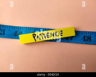 The image shows the word Patience written on a yellow sticky note placed on a blue measuring tape. Stock Photo