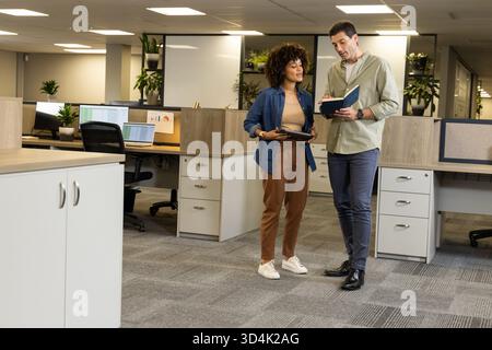 Discussing Diverse coworkers reviewing project plans in open-plan office, with tablet and notebook Stock Photo