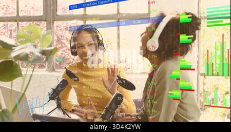 Recording two women co-hosts wearing mustard top and light sweater at loft with mics laptop charts Stock Photo
