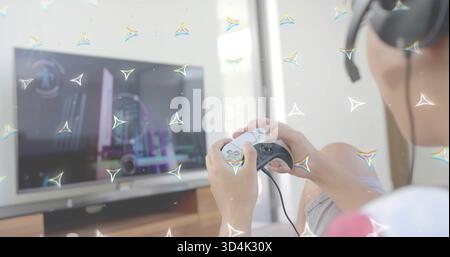 Playing casual Asian man holding wired controller wearing headphones on sofa with TV, copy space Stock Photo
