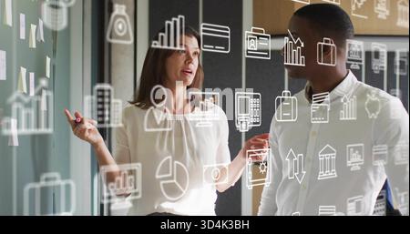 Pointing pair in white shirts discussing at office glassboard, with pink marker and sticky notes Stock Photo