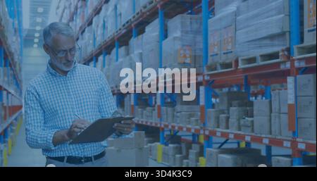 Inspecting senior manager in checked shirt and glasses checking clipboard in warehouse, copy space Stock Photo
