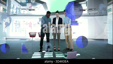 Reviewing three professionals in business attire pointing at charts on carpet with tablets, laptop Stock Photo