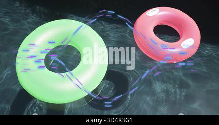 Floating neon green and pink rings, white handles on dark pool casting purple or blue trails, causti Stock Photo