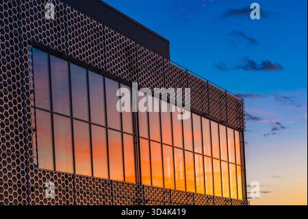 Vibrant hues of orange and purple light up the sky as the sun sets behind a modern building in Molndal. The windows beautifully capture the changing c Stock Photo
