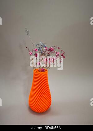 Orange Art object vase printed on 3D printer from melted orange plastic with colorful flowers. progressive technology 3D printing recycling Stock Photo
