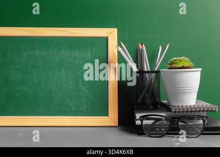 Classroom blackboard with pencils, plant and eyeglasses on a teacher's desk Stock Photo