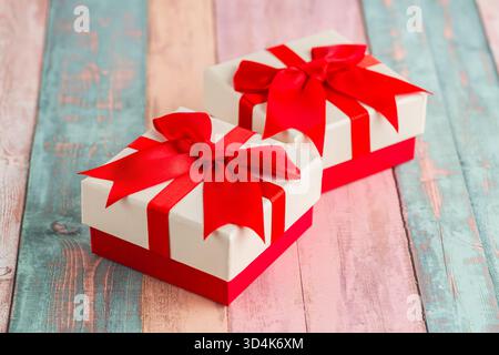 Two gift boxes with ribbons on colorful wooden background. White and red gift boxes with white ribbons close-up image. Stock Photo