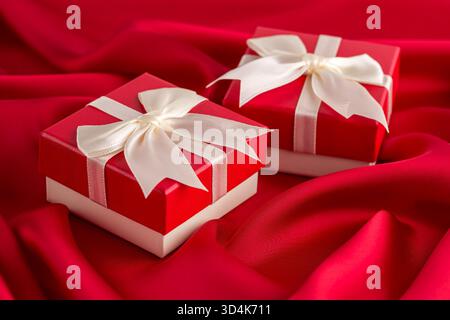 Two red and white gift boxes with ribbon on red silk background. Stock Photo