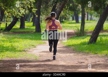 Rear view shot of woman running outdoors in park wearing sportswear and smiling Stock Photo