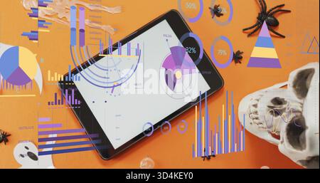 Showing black tablet presenting charts on orange desk, with skull, spiders and marbles Stock Photo