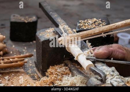 Traditional woodturner carving wooden pieces by hand and food in a Moroccan souk. Artisanal woodturning, with shavings and handcrafted details. Stock Photo