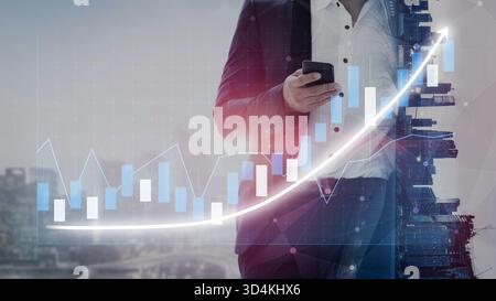 A businessman in a suit holds a smartphone against a city backdrop, with a financial growth graph overlay, symbolizing progress in the modern business Stock Photo