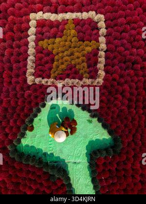Aerial view of a vibrant display featuring a golden star within a square and a green arrow pointing upwards amidst a sea of red, Quang Phu Cau, Hanoi, Stock Photo
