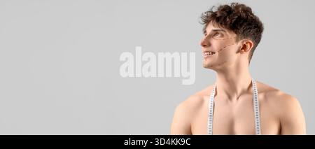 Young man with markings on his face and measuring tape against grey background with space for text. Plastic surgery concept Stock Photo