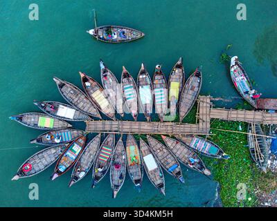 Dhaka, Bangladesh - 26 October 2025: Aerial view of fishing boats docked near a bamboo pier, their colorful interiors contrasting with the teal river Stock Photo