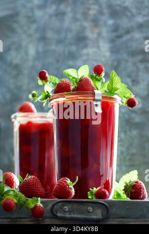 Two preserving jars filled with homemade strawberry jam and fresh strawberries decorated on a gray metal background Stock Photo