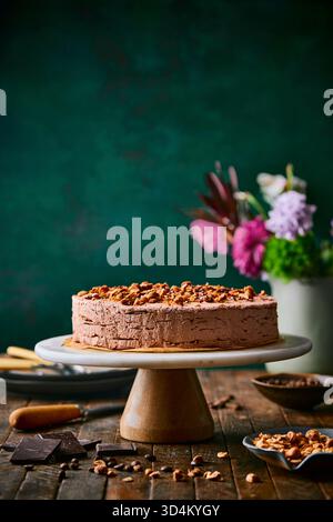 Side angle of a decadent chocolate cake sprinkled with hazelnuts on a marble cake stand against a rich, moody custom green backdrop. Stock Photo