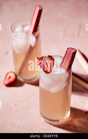 Two glasses of pink sparkling water garnished with rhubarb and strawberries against a pink background. Stock Photo