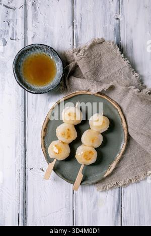 Top view Japanese dango dumplings on ceramic plate with tea bowl wooden sticks linen napkin on white wooden background. Traditional Asian dessert Stock Photo