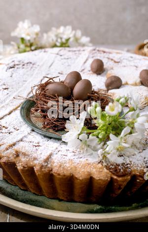 Homemade Easter tart Pastiera Napolitano with powdered sugar topped with chocolate eggs nest and white spring flowers. Traditional festive dessert on Stock Photo